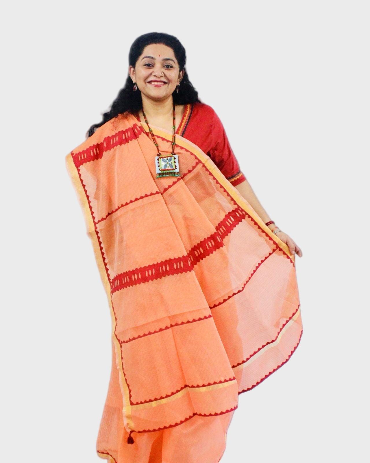 A woman showcasing a Kota Doriya Cotton Saree with orange and red color scheme and applique detailing.