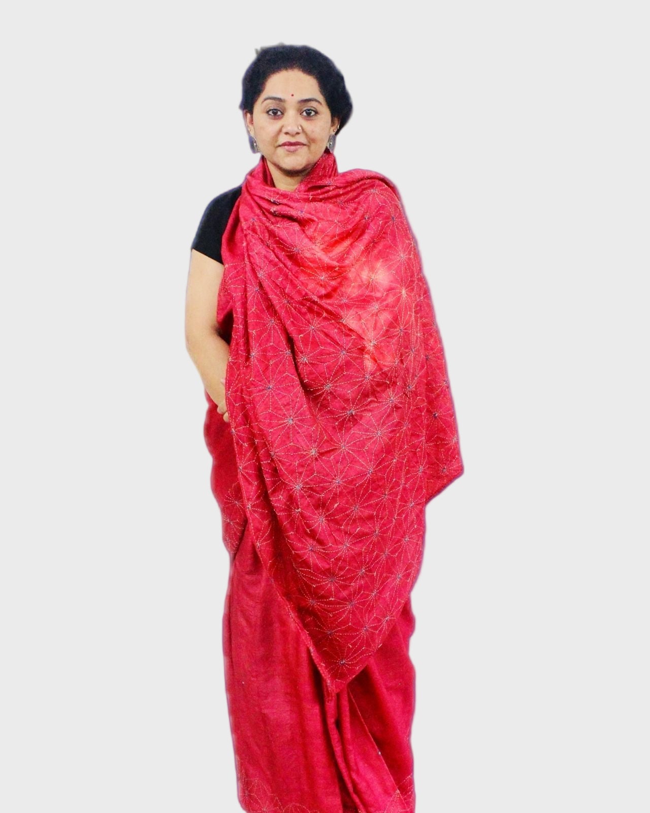 A woman showcasing a handcrafted red Tanka silk saree with floral hand embroidery details.
