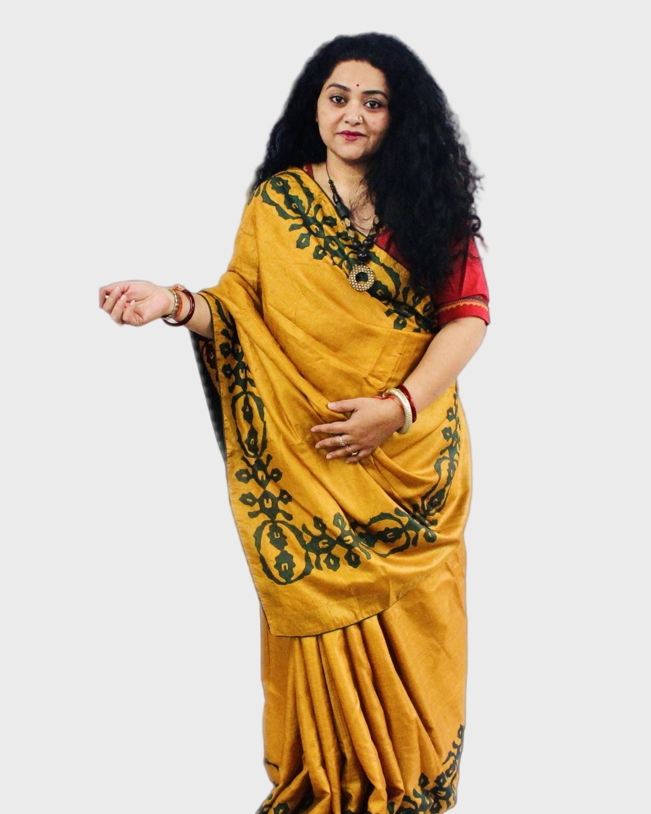 A woman showcasing a golden yellow silk saree with green applique work.