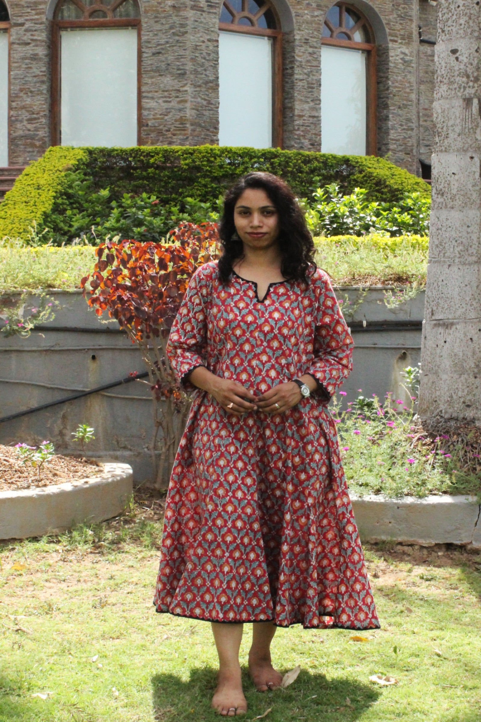 Woman wearing handcrafted red floral A-line cotton dress with block print and three-quarter sleeves outdoors.