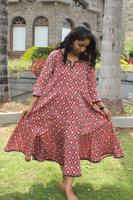 Woman wearing handcrafted red floral A-line cotton dress with block print and three-quarter sleeves outdoors.