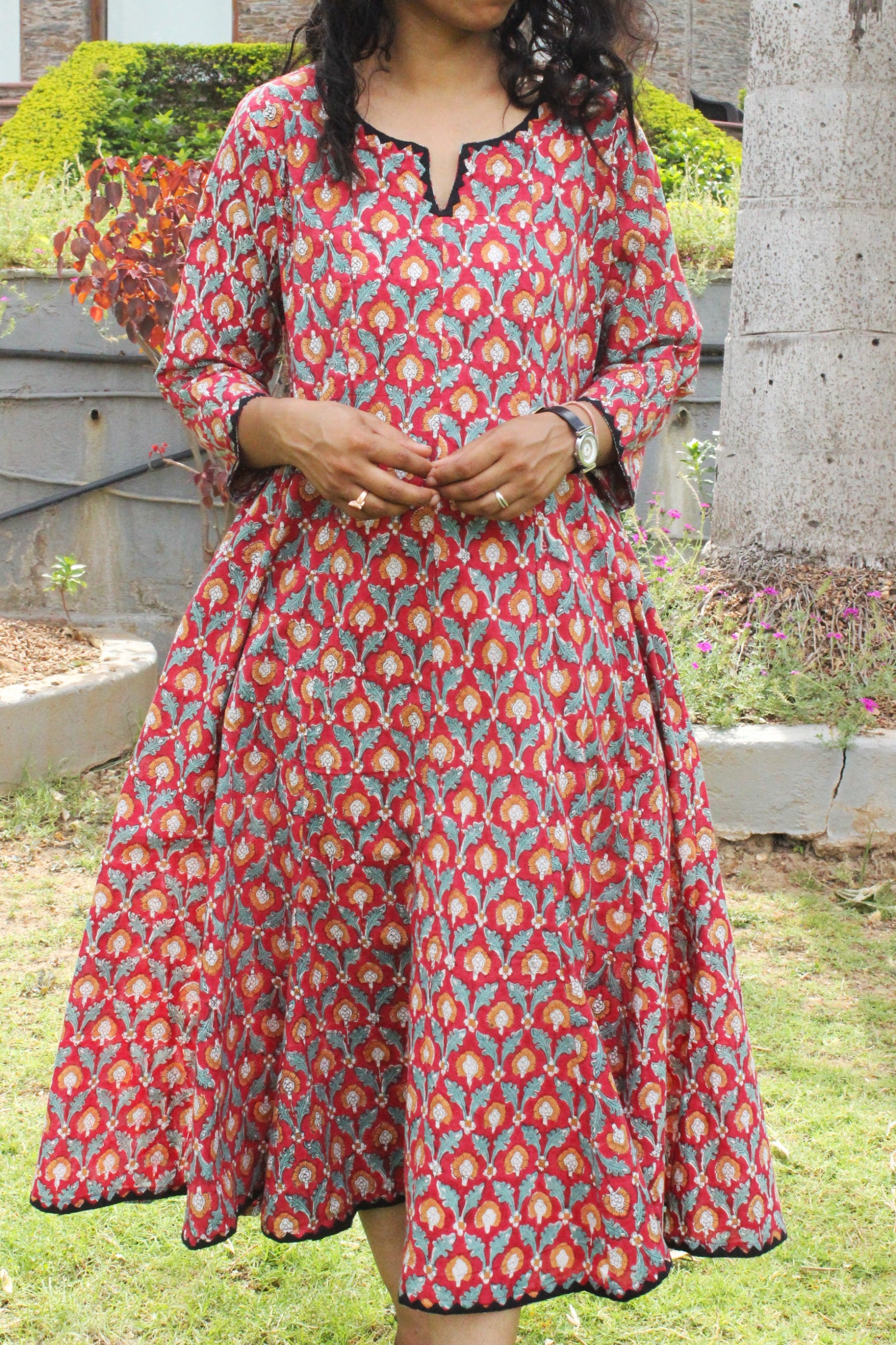 Woman wearing handcrafted red floral A-line cotton dress with block print and three-quarter sleeves outdoors.