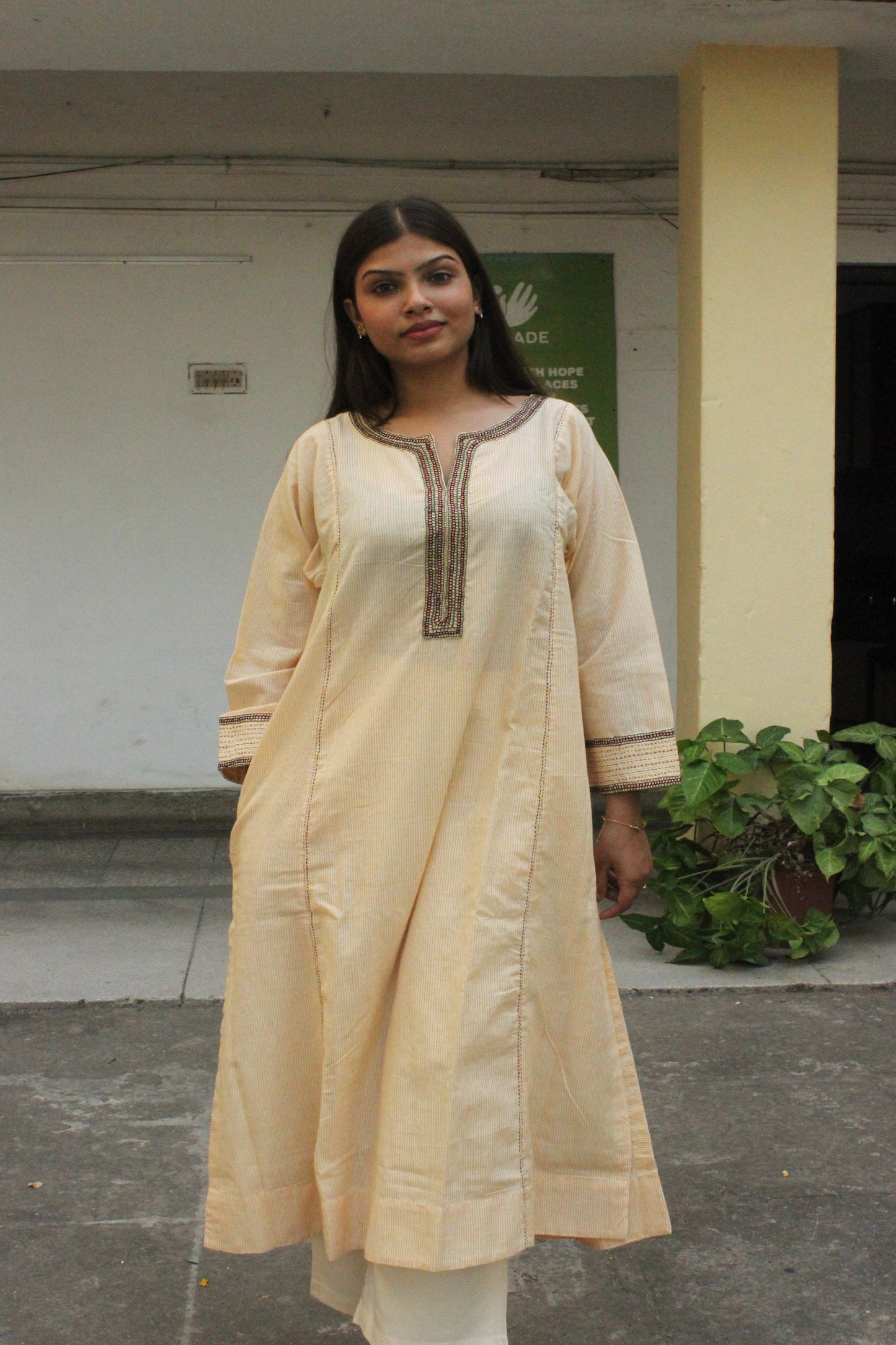 Woman wearing handcrafted striped beige cotton A-line kurta with hand embroidery and three-quarter sleeves.