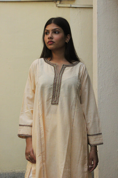 Woman wearing handcrafted striped beige cotton A-line kurta with hand embroidery and three-quarter sleeves.