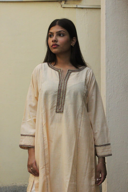 Woman wearing handcrafted striped beige cotton A-line kurta with hand embroidery and three-quarter sleeves.