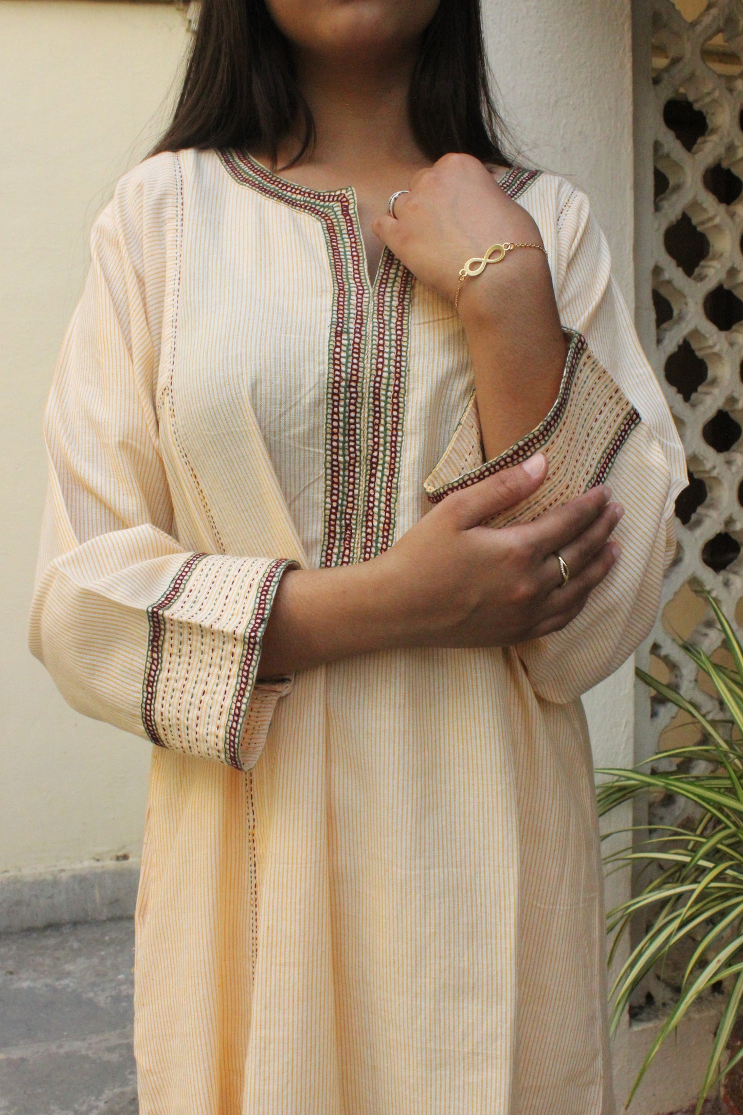 Woman wearing handcrafted striped beige cotton A-line kurta with hand embroidery and three-quarter sleeves.