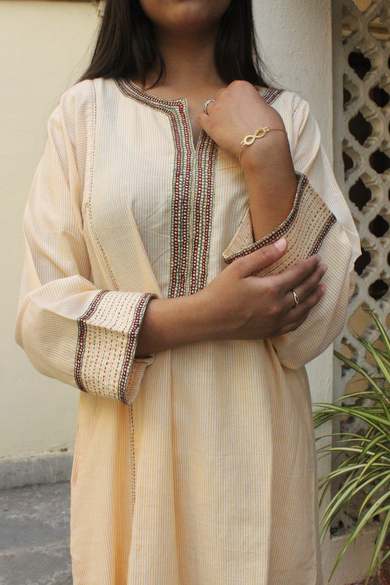 Woman wearing handcrafted striped beige cotton A-line kurta with hand embroidery and three-quarter sleeves.