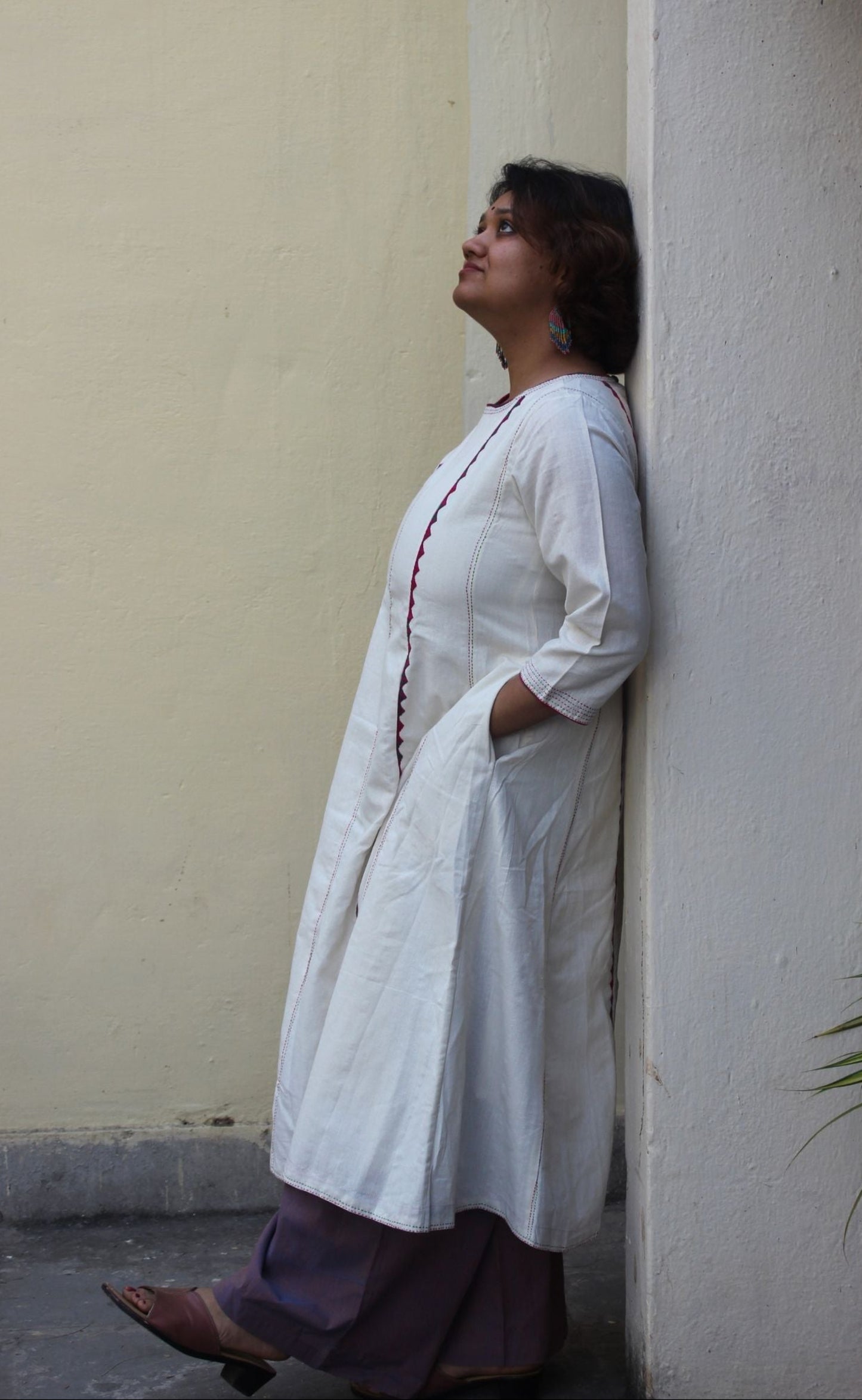 Front view of a white handcrafted appliqué cotton A-line kurta with side pockets on a model.
