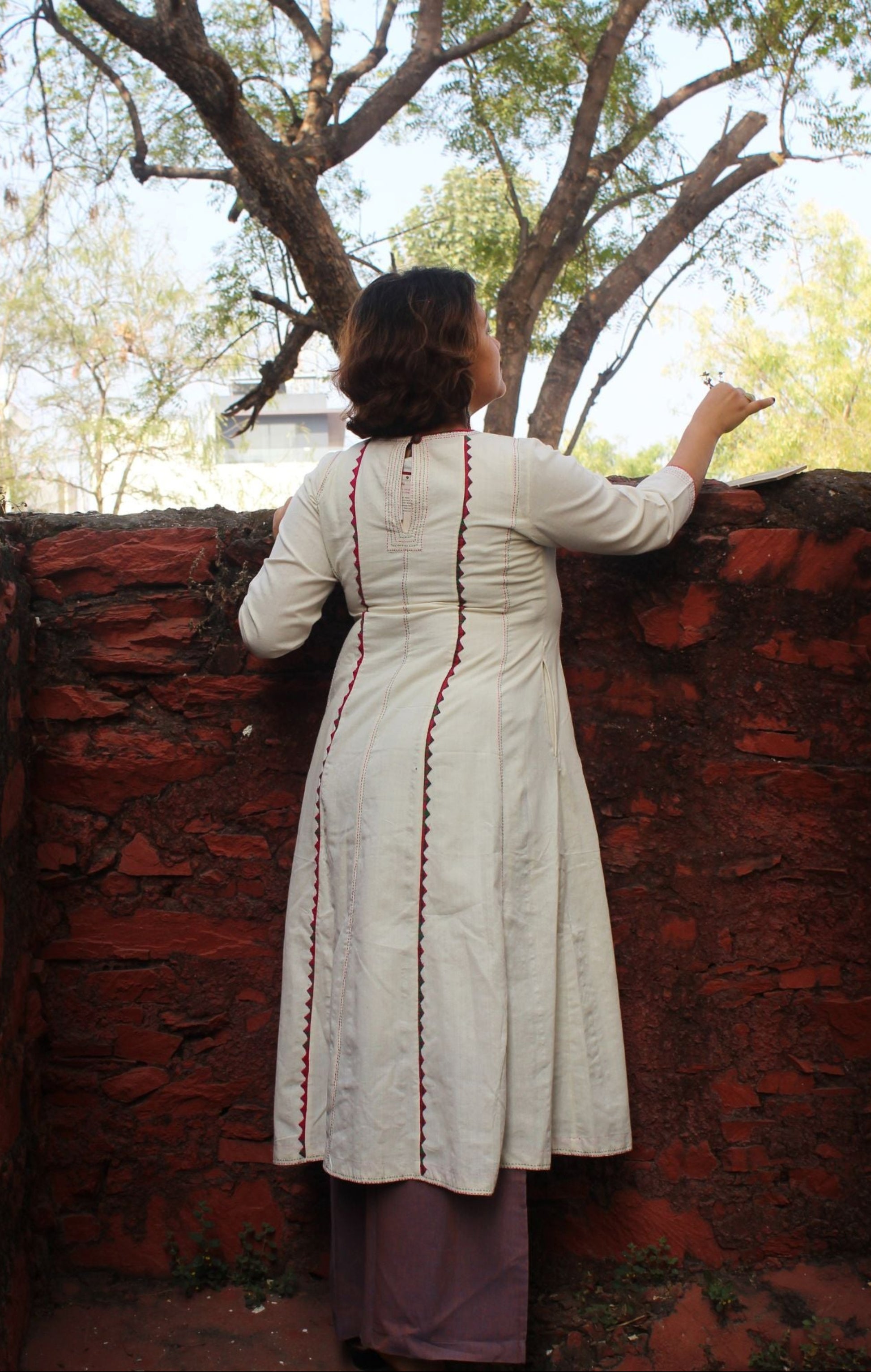 Front view of a white handcrafted appliqué cotton A-line kurta with side pockets on a model.