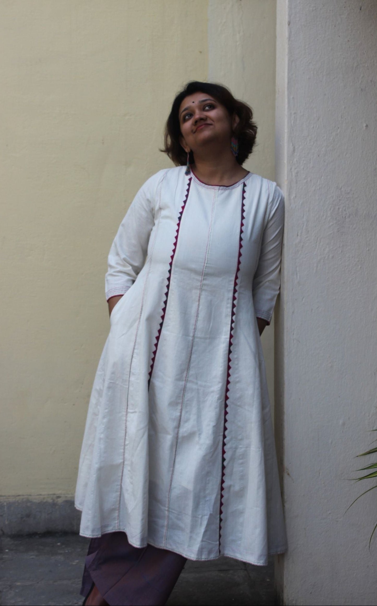 Front view of a white handcrafted appliqué cotton A-line kurta with side pockets on a model.